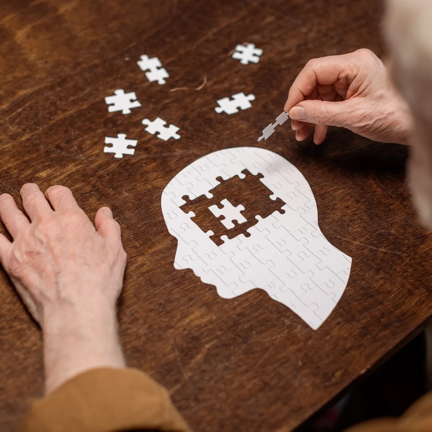 Ein älterer Mann legt an einem Holztisch ein Puzzle in Form eines Kopfes